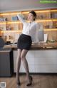 A woman in a white shirt and black skirt posing in front of a desk.