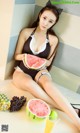 A woman sitting on the floor holding a slice of watermelon.