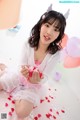 A young woman sitting on the floor holding a bunch of balloons.