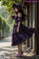 A woman in a purple dress and hat standing on a sidewalk.